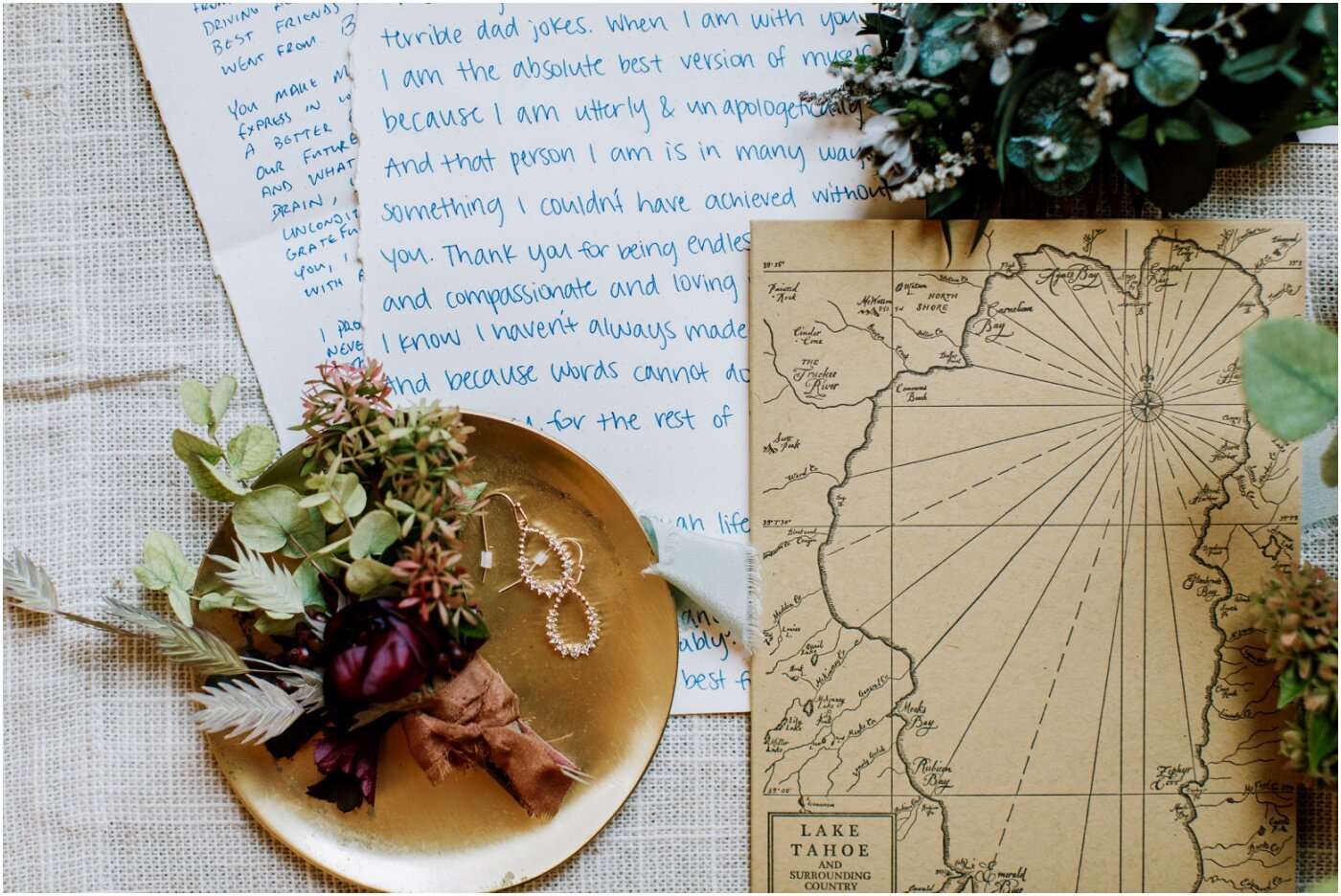 flat lay photo of wedding details, boutonniere, map, love letter, wedding rings